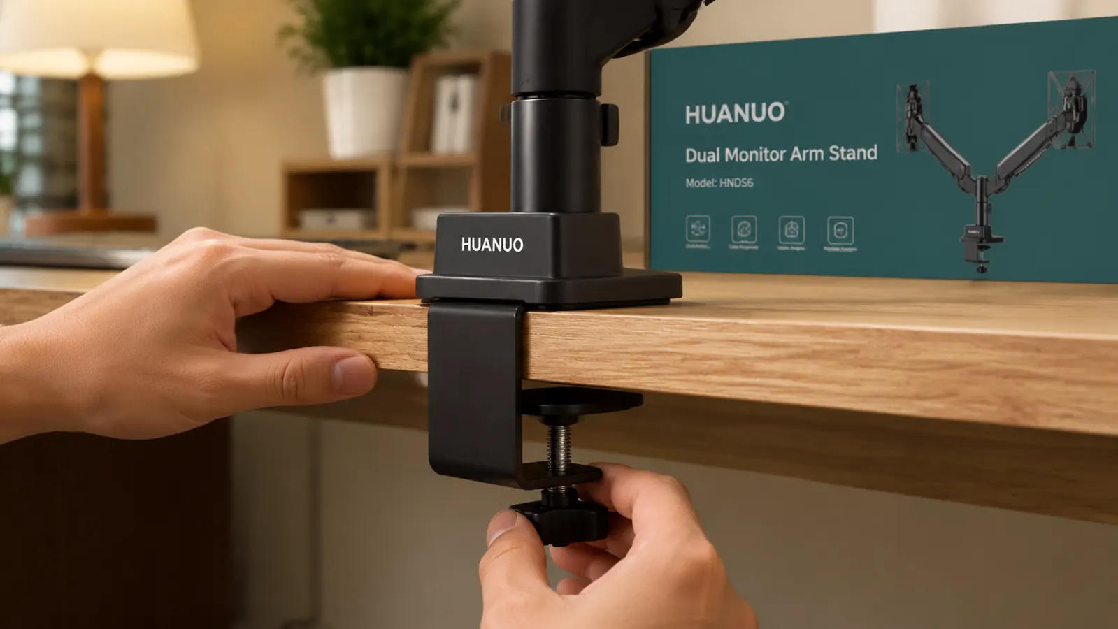 Hands tightening the C-clamp screw on a monitor arm mounted to the edge of a wooden desk